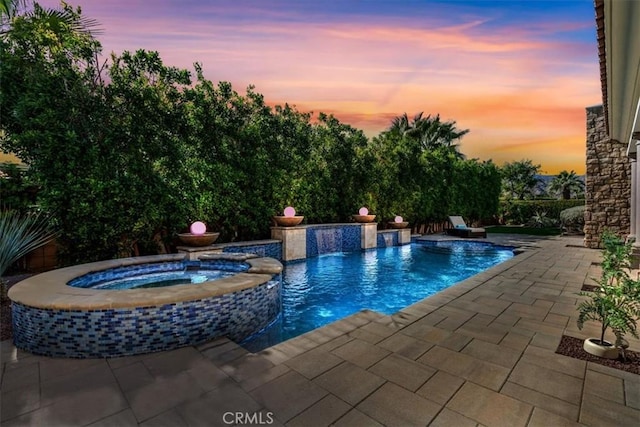 pool at dusk with a patio and a pool with connected hot tub