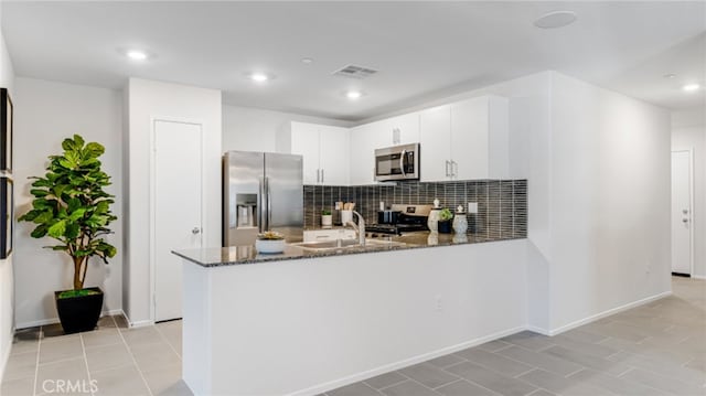 kitchen featuring stainless steel appliances, a peninsula, visible vents, backsplash, and dark stone counters