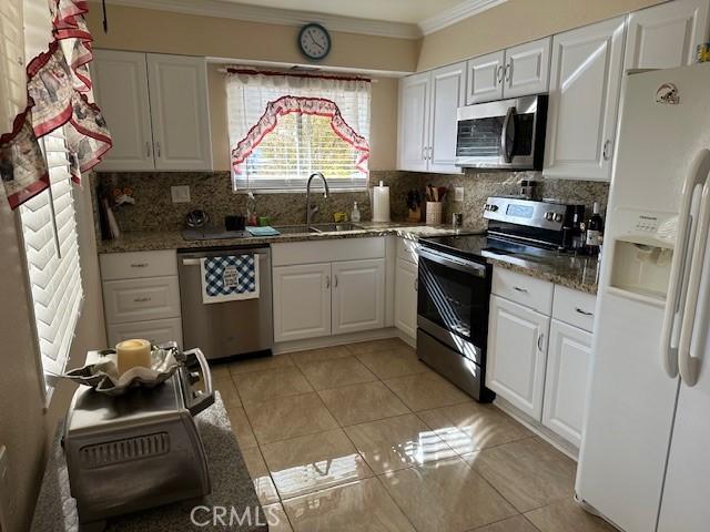 kitchen featuring stainless steel appliances, a sink, white cabinets, backsplash, and crown molding