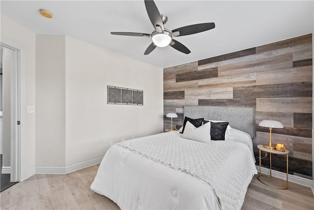 bedroom with an accent wall, wood walls, a ceiling fan, baseboards, and light wood-type flooring