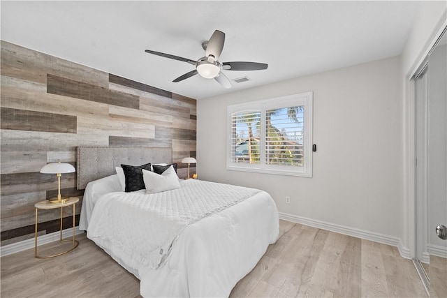 bedroom featuring light wood-type flooring, baseboards, an accent wall, and visible vents