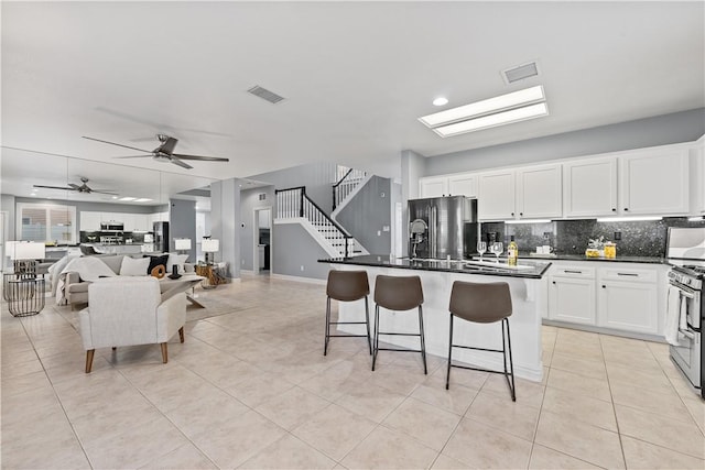 kitchen with dark countertops, visible vents, open floor plan, white cabinetry, and a kitchen bar