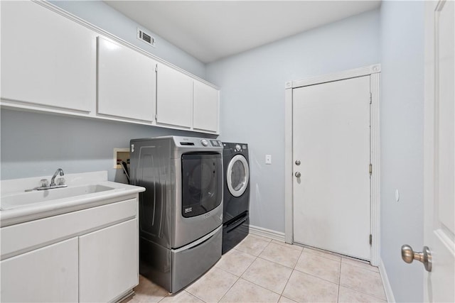 washroom with cabinet space, visible vents, washing machine and dryer, a sink, and light tile patterned flooring