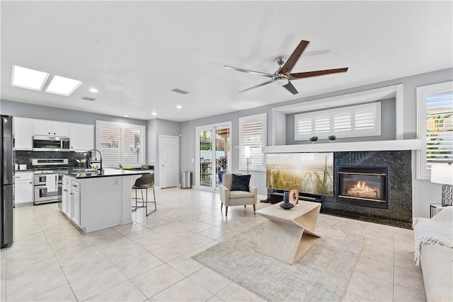 kitchen with stainless steel appliances, dark countertops, white cabinetry, a sink, and a kitchen breakfast bar