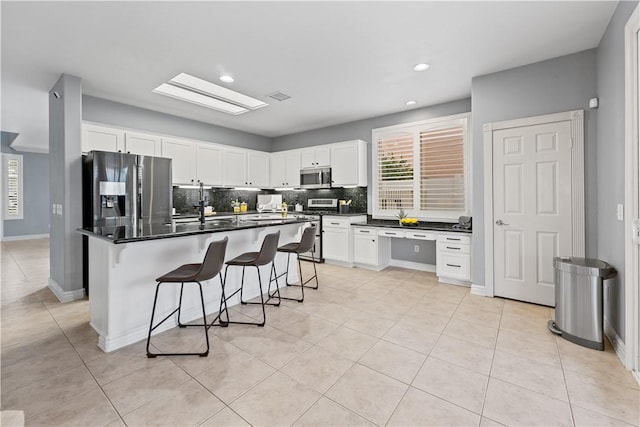 kitchen with a center island, stainless steel appliances, dark countertops, white cabinetry, and a kitchen breakfast bar