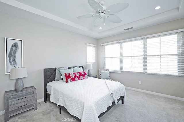 bedroom with a tray ceiling, light colored carpet, visible vents, and baseboards