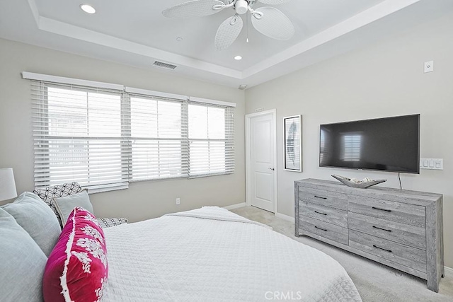 bedroom featuring a tray ceiling, visible vents, light carpet, and baseboards