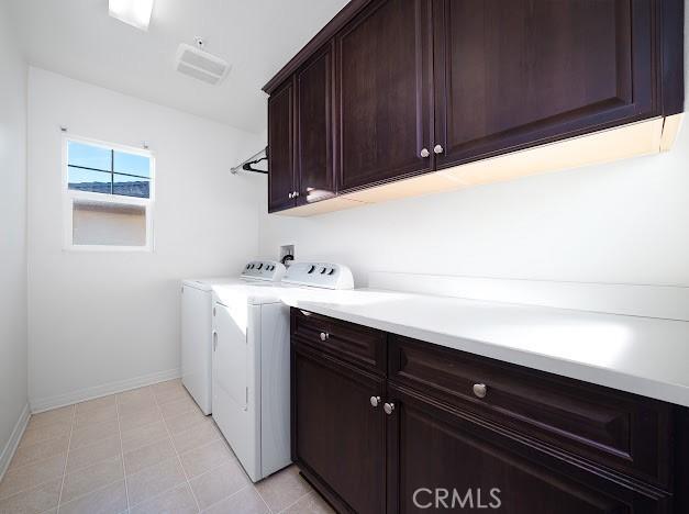 laundry area featuring cabinet space, light tile patterned floors, baseboards, and washing machine and clothes dryer