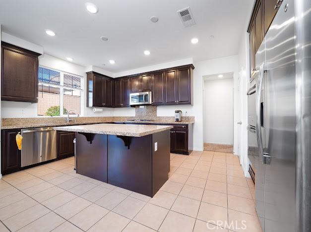 kitchen featuring dark brown cabinetry, visible vents, a kitchen island, stainless steel appliances, and a kitchen bar