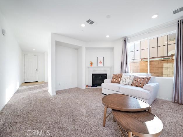 living room featuring light colored carpet, a glass covered fireplace, visible vents, and recessed lighting