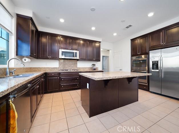 kitchen with a breakfast bar area, light tile patterned floors, stainless steel appliances, visible vents, and a sink