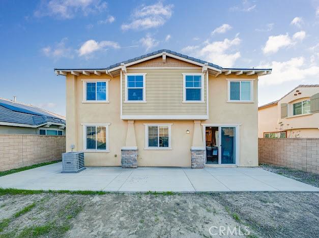 rear view of house with stucco siding, a fenced backyard, cooling unit, and a patio