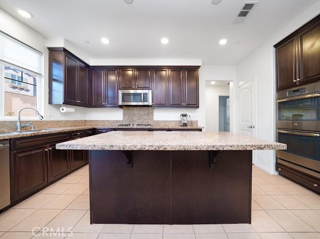 kitchen with visible vents, a kitchen island, a kitchen breakfast bar, stainless steel appliances, and a sink