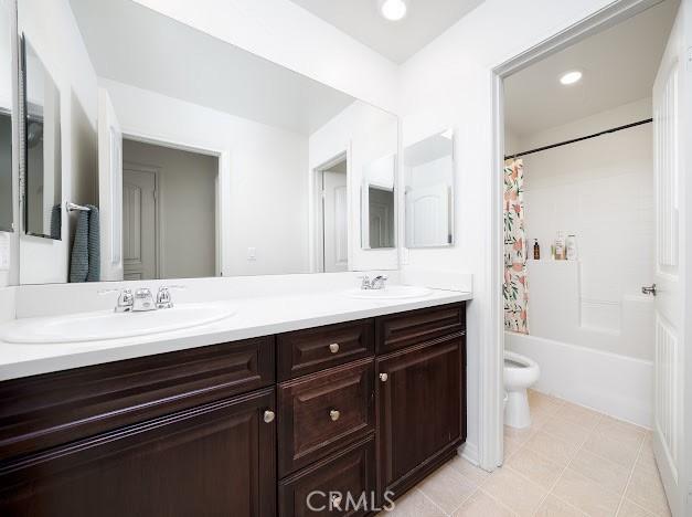 bathroom featuring shower / bath combination with curtain, double vanity, a sink, and toilet