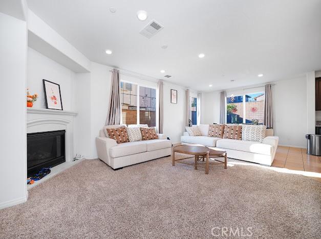 living room featuring light carpet, a glass covered fireplace, visible vents, and recessed lighting