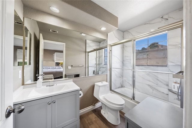 ensuite bathroom with connected bathroom, toilet, wood finished floors, vanity, and a shower with door