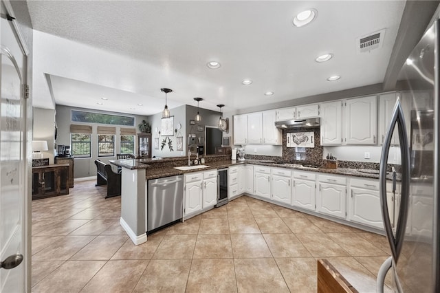 kitchen with hanging light fixtures, appliances with stainless steel finishes, white cabinets, beverage cooler, and a peninsula