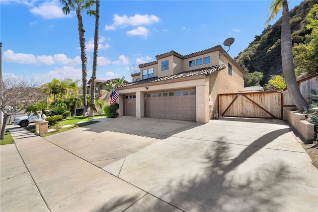 mediterranean / spanish-style house featuring a garage, concrete driveway, a tiled roof, a gate, and stucco siding