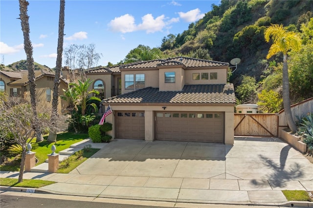 mediterranean / spanish house with concrete driveway, fence, a tile roof, and stucco siding