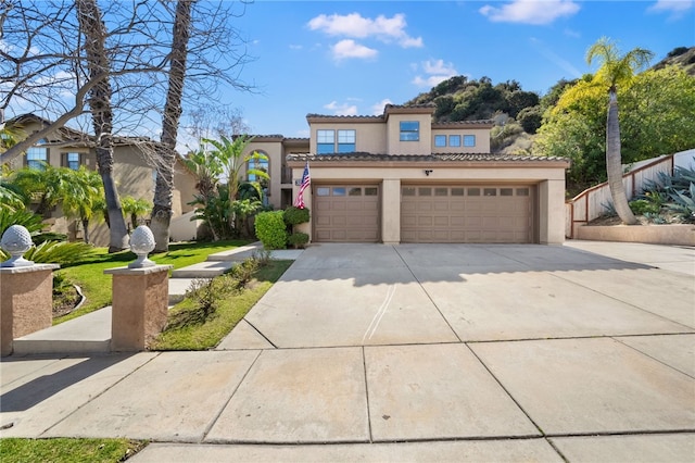 mediterranean / spanish-style house with a garage, concrete driveway, a tile roof, and stucco siding