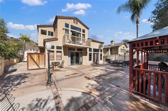 rear view of property with a patio, a tile roof, fence, a gazebo, and stucco siding