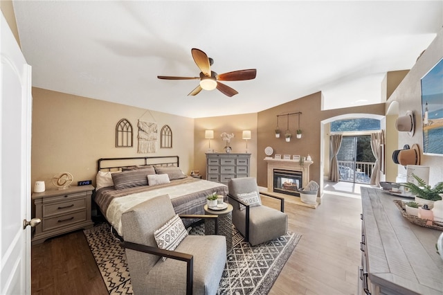 bedroom featuring ceiling fan, access to outside, light wood-style flooring, and a glass covered fireplace