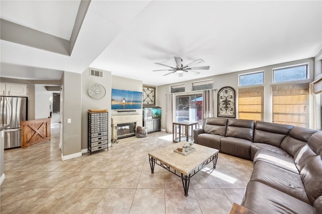 living room with light tile patterned floors, visible vents, baseboards, a ceiling fan, and a glass covered fireplace