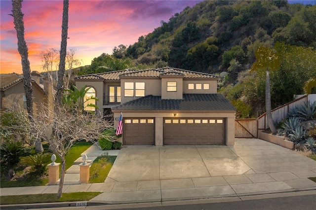 mediterranean / spanish house featuring concrete driveway, a tile roof, fence, and stucco siding