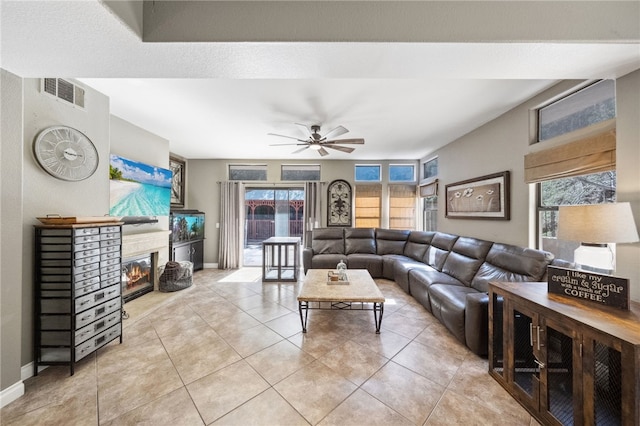 living room featuring light tile patterned floors, baseboards, visible vents, a ceiling fan, and a glass covered fireplace