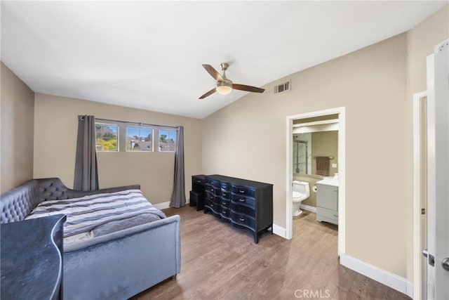 bedroom with visible vents, baseboards, lofted ceiling, wood finished floors, and ensuite bathroom