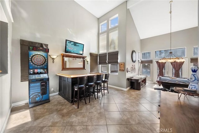 bar featuring high vaulted ceiling, tile patterned flooring, indoor bar, baseboards, and hanging light fixtures