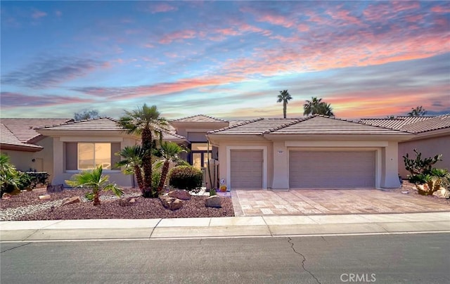 view of front of property with a garage, a tile roof, decorative driveway, and stucco siding