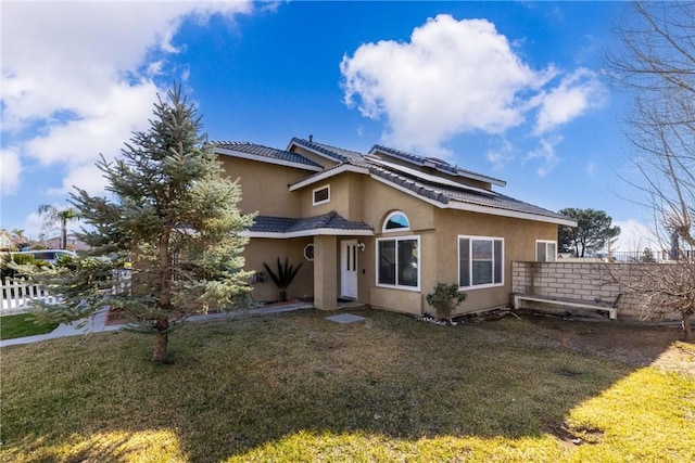 view of front of house with a tile roof, fence, a front lawn, and stucco siding