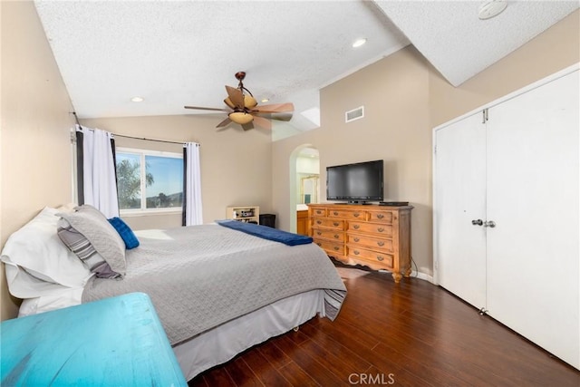 bedroom with arched walkways, dark wood finished floors, lofted ceiling, visible vents, and a textured ceiling