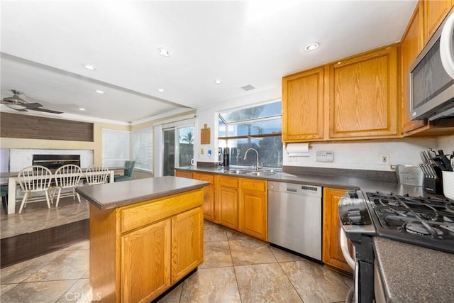 kitchen featuring a center island, stainless steel appliances, dark countertops, a sink, and ceiling fan