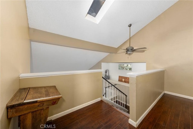 corridor with dark wood-style floors, vaulted ceiling with skylight, baseboards, and an upstairs landing