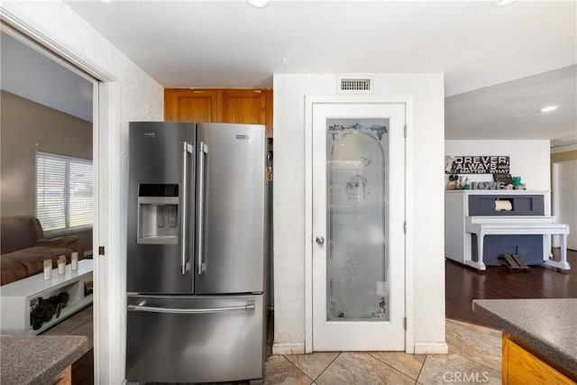 kitchen with high end refrigerator, visible vents, dark countertops, brown cabinets, and light tile patterned flooring