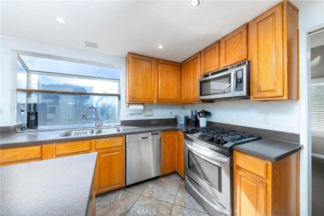 kitchen featuring stainless steel appliances, dark countertops, recessed lighting, brown cabinetry, and a sink