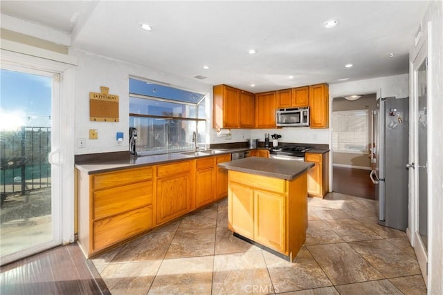 kitchen with dark countertops, a kitchen island, stainless steel appliances, a sink, and recessed lighting