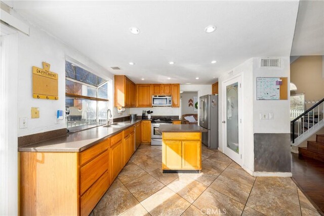 kitchen featuring visible vents, dark countertops, a kitchen island, stainless steel appliances, and a sink