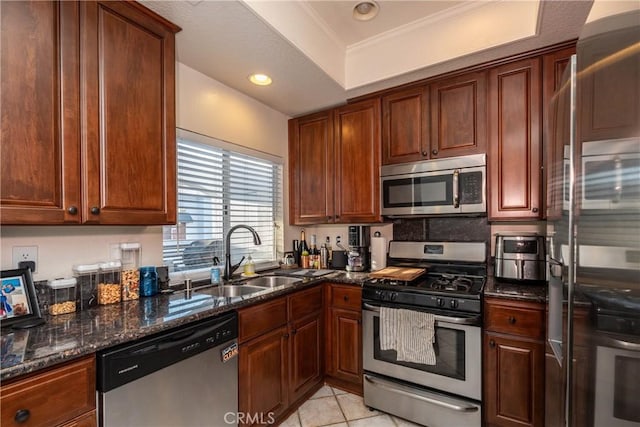 kitchen featuring light tile patterned floors, dark stone countertops, a tray ceiling, stainless steel appliances, and a sink