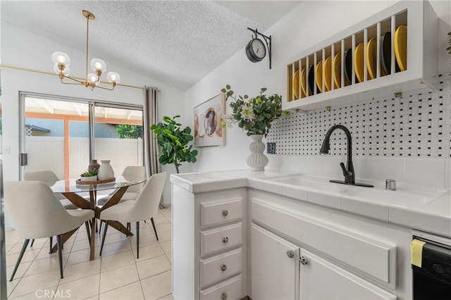 kitchen with white cabinets, tile countertops, lofted ceiling, hanging light fixtures, and a sink