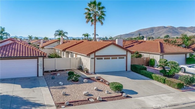 mediterranean / spanish-style home with fence, a mountain view, concrete driveway, and a tiled roof