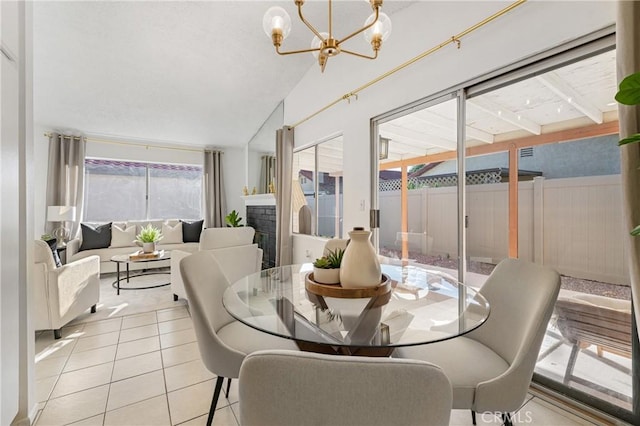 dining area with lofted ceiling, light tile patterned flooring, a glass covered fireplace, and a notable chandelier