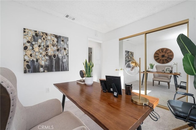 home office with carpet, visible vents, and a textured ceiling