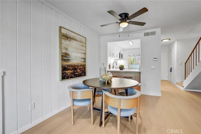 dining space featuring visible vents, a ceiling fan, stairs, and light wood-style floors