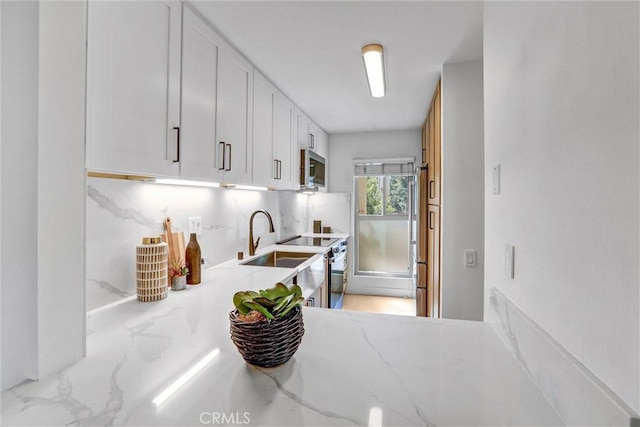 kitchen with tasteful backsplash, stainless steel microwave, light stone countertops, range with electric stovetop, and white cabinets