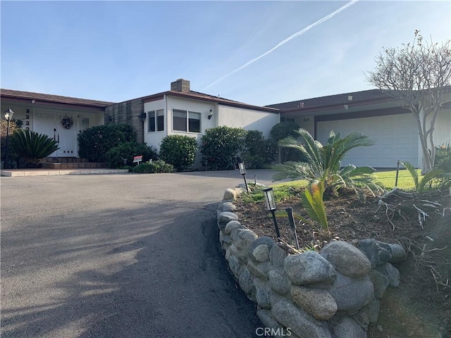 ranch-style home with stucco siding, an attached garage, a chimney, and concrete driveway