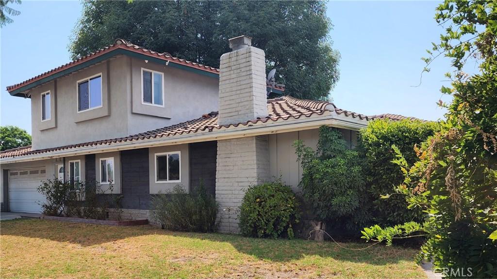 view of side of property featuring an attached garage, a chimney, a lawn, and a tiled roof