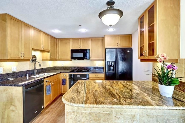 kitchen featuring dark stone countertops, a textured ceiling, light wood-type flooring, black appliances, and a sink